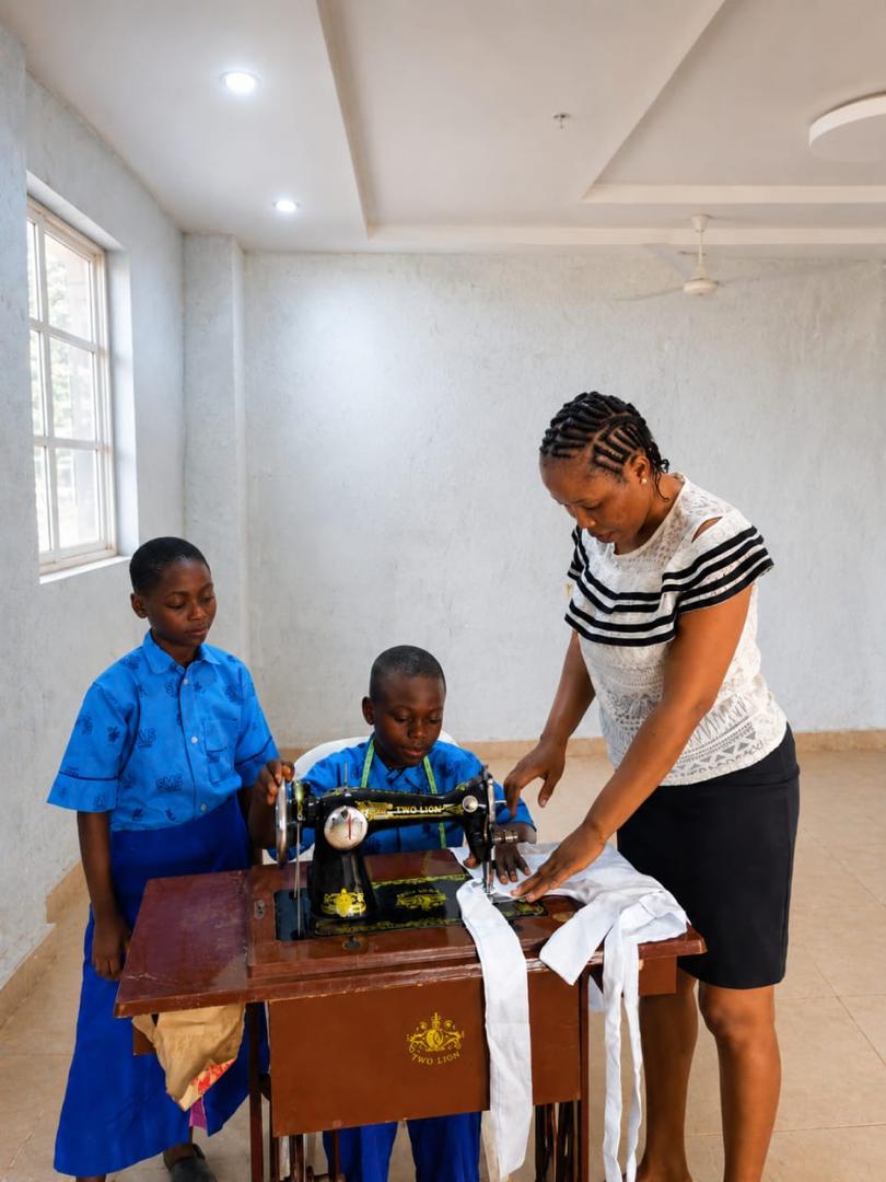 A teacher guiding two students using a sewing machine in a practical skills lesson
