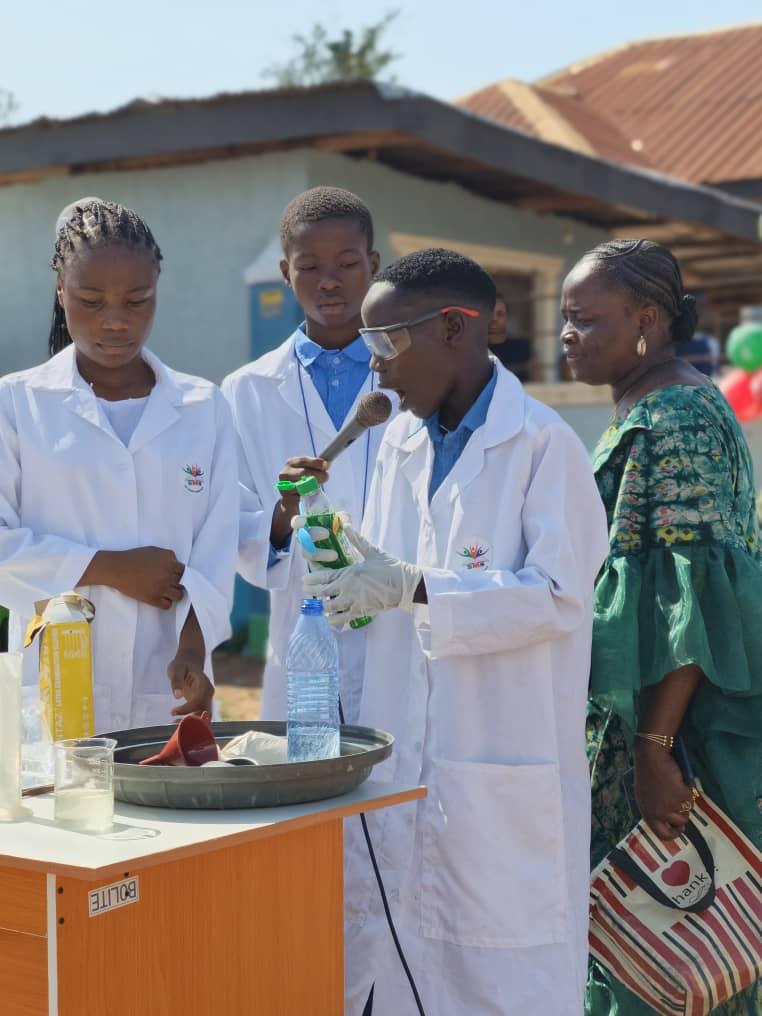 Secondary students in lab coats presenting a science experiment to visitors