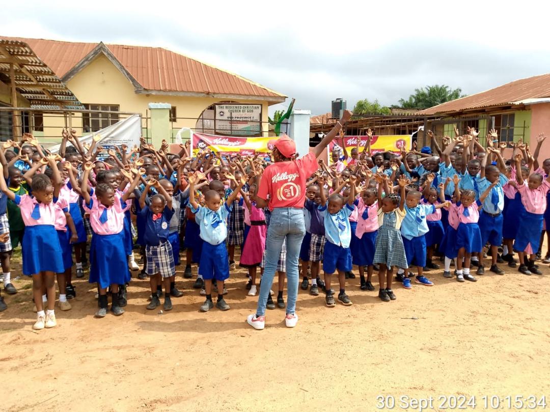 Primary pupils of Sound Mind Schools raising their hands during an outdoor assembly activity